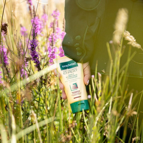 Hand holding Gerovital Hair Expert Keratin Regenerating Hair Mask among grass and purple flowers