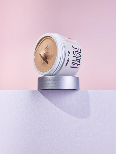 Open Gerovital Must Have moisturising cream jar with beige cream balanced on its silver lid against pink