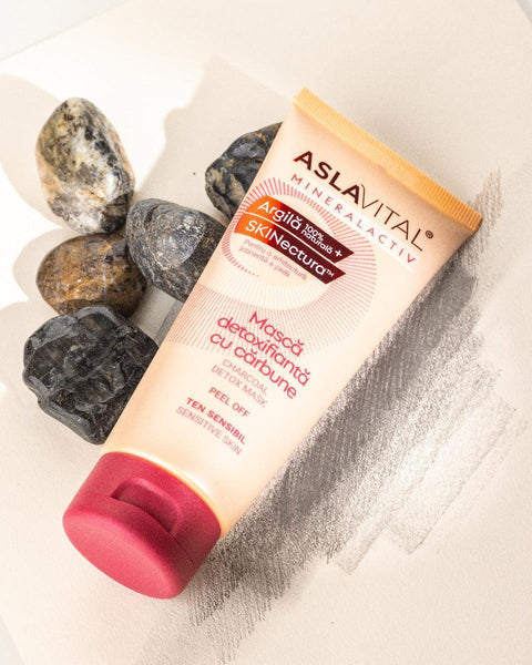 Aslavital Charcoal Detox Peel-Off Mask tube beside dark stones and clay powder