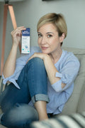 Woman seated on a sofa holding a box of Gerovital H3 Classic Eyes and Lips Contour Cream