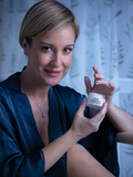 Woman holding an open Gerovital H3 Classic night cream jar with cream on her fingertip