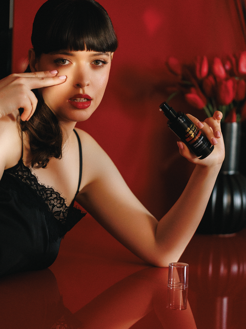 Woman holding Gerovital Premium cream bottle with fingers beside her cheek against red