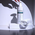 Hand pressing Gerovital Body Sculpting Massage Oil pump beside rolled towel