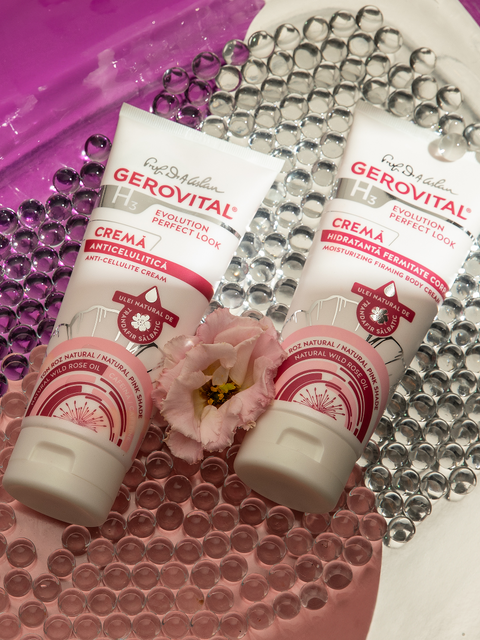 Gerovital Anti Cellulite Cream and Moisturising Firming Body Cream tubes on glass beads beside a pink flower