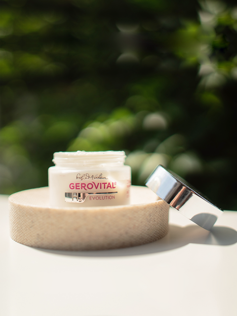 Open Gerovital H3 Evolution cream jar on a round wooden stand with silver lid beside it