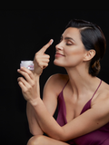 Woman holding an open Gerovital cream jar with cream on her raised fingertip