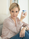 Woman holding a Gerovital H3 Retinol Wrinkle Prevention Cream jar beside her face