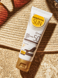Gerovital Sun Tinted Face Cream SPF 50 tube on sand beside straw hat and sunglasses